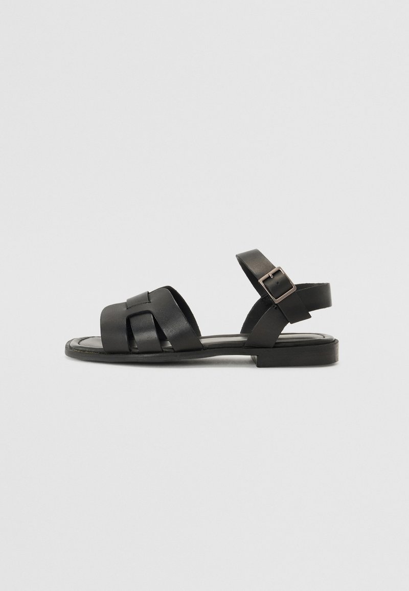 Must mustränd, millel on lame tall ja ristuvad rihmad ning ankle strap, millel on klamber. Sile tekstuur ja minimaalne disain.