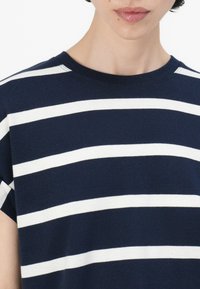 Marinblå og hvit stripete t-skjorte, laget av bomull, med rund halsdesign, korte ermer, og har horisontale striper av varierende bredde.