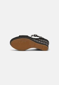 Sandale compensée noire avec semelle en caoutchouc marron, bride de cheville avec boucle et motif blanc tacheté sur le talon compensé.