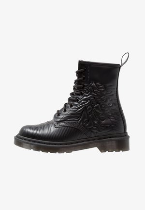 Stivale alla caviglia nero con tomaia testurizzata caratterizzata da motivi ondulati e a costine, punta rinforzata e suola in gomma. Anello a tirante sul tallone.