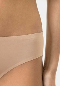 Beige nahtlose Unterwäsche mit glatter Textur und breitem elastischem Bund, in einer Nahaufnahme auf der Haut dargestellt.