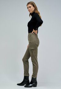 Pantalons cargo olive cintrés avec poches avant et latérales, associés à un haut à manches longues noir et à des bottines noires. Design simple et minimaliste.