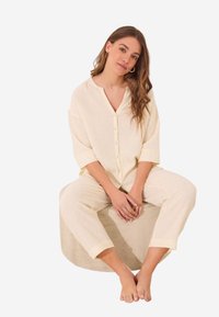 Lichtgele, button-up pyjama set met korte mouwen en cropped broek, voorzien van kleine, subtiele stippen. Zacht stof met een comfortabele pasvorm.
