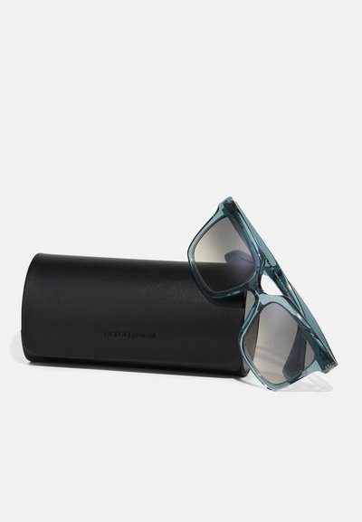 O pereche de ochelari de soare teal cu rame pătrate, așezată pe un etui rigid negru, cu textul gravat "Giorgio Armani."