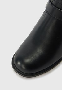 Μαύρη δερμάτινη μπότες με λεία φινίρισμα, στρογγυλή μύτη και διακριτές λεπτομέρειες ραφής. Η σ�όλα είναι επίπεδη με ελαφρά ανύψωση στη μύτη.