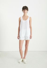 Valge lina tank top, millel on ümar kaelus ja lahtine istuvus, koos valgete triibuliste lühkatetega. Mudel kannab kreemivärvi tossusid. Lihtne ja kerge.