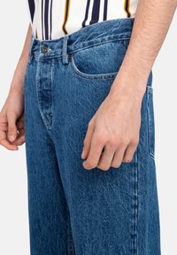 Vaqueros de denim azul de talle alto con un acabado desgastado, que cuentan con un cierre de botón, cinco bolsillos y un corte recto.