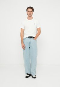 Biele bavlnené tričko s malým logom, svetlomodré široké džínsové nohavice, čierny opasok a čierno-biele topánky. Jednoduchý a neformálny outfit.