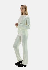 Ensemble de vêtements d'intérieur en maille de couleur blanc cassé, avec une texture côtelée, des manches larges et un pantalon droit. Associé à des chaussures noires épaisses.