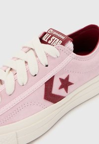 Sneaker in camoscio rosa chiaro con lacci bianchi, caratterizzato da un logo bordeaux e accenti a forma di stella, e una suola in gomma con dettagli di cucitura sottili.