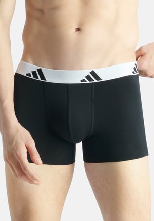 Schwarze Boxer-Shorts aus dehnbarem Material, mit einem weißen elastischen Bund, der schwarze Markenlogo-Details aufweist, und einem figurbetonten Design.