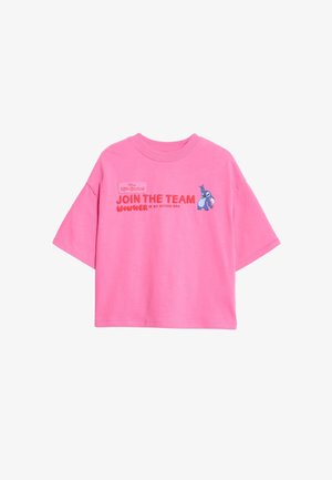 Różowy t-shirt z krótkim rękawem z haftowanym napisem i logo Disney, zestawiony z dużymi różowymi okularami przeciwsłonecznymi i teksturowanymi kręconymi włosami.