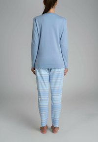 Top a maniche lunghe di un blu chiaro abbinato a pantaloni da pigiama blu e bianchi con motivi geometrici e righe orizzontali.