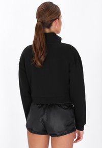 Hanorac negru decupat cu guler înalt și croială supradimensionată, asortat cu pantaloni scurți negri lucioși. Textură netedă și detaliu cu talie elastică.