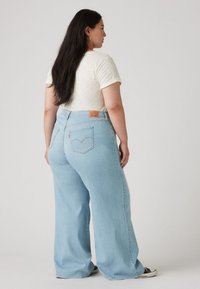 Light blue wide-leg jeans made of denim, featuring two back pockets and a brown leather brand patch at the waistband.