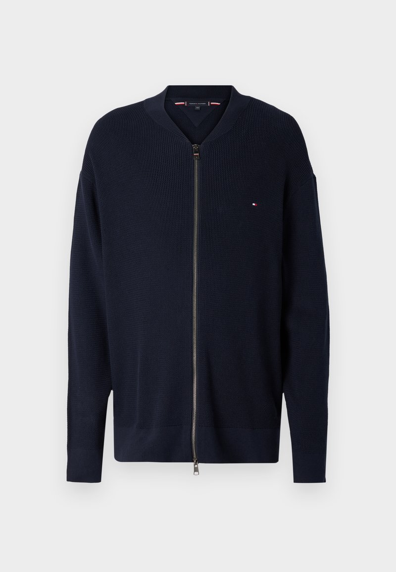 Navy blue zip cardigan made of textured fabric with a ribbed design. Features a zip closure and a small logo on the chest.