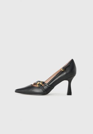 Scarpa nera in pelle con tacco alto e punta affusolata, caratterizzata da dettagli in metallo color oro e un design con ritagli sui lati.