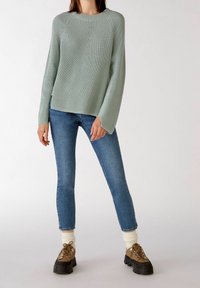 Light green ribbed knitted sweater with long sleeves, paired with fitted blue jeans. Chunky brown shoes and cream-colored ankle socks complete the look.