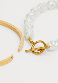 Gold-tone metal cuff and a chunky pearl bracelet with a circular toggle clasp. Smooth, shiny surfaces and irregular pearl shapes.