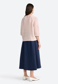 Pull en rose clair texturé avec des manches trois-quarts, associé à une jupe bleu marine avec une longueur de patte au-dessus de la cheville et des chaussures blanches.