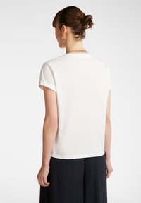 T-shirt blanc à manches courtes avec un col rond, texture lisse et coupe décontractée. Porté avec un pantalon sombre et fluide.