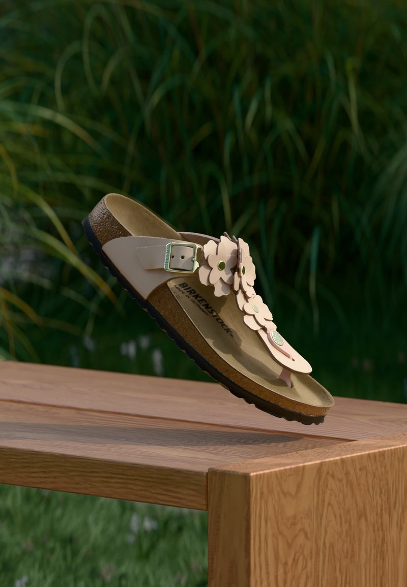 Μπεζ σανδάλι Birkenstock με λουλουδένιες διακοσμήσεις, αιωρούμενο πάνω από ένα ξύλινο παγκάκι με φόντο πράσινα φυτά σε εξωτερικό χώρο.