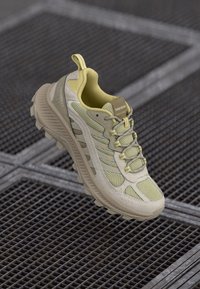 Light yellow hiking shoe with a mesh and synthetic upper, cushioned sole, and textured accents. Features lacing system and reinforced heel.