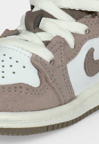 Κοντινή εικόνα ενός μπεζ και λευκού αθλητικού παπουτσιού με χοντρές λευκές κορδόνια, διάτρητη μύτη, υφή σουέντ και δέρματος και λεπτομέρεια από λαστιχένια σόλα.