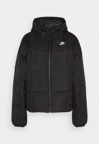 Doudoune noire avec capuche. Présente un design matelassé, une fermeture éclair à l'avant, des poignets élastiques et un petit logo Nike blanc en haut à gauche.