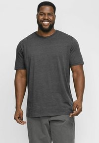 Camiseta de manga corta en gris oscuro, hecha de un tejido suave, con un cuello redondo y un corte relajado, combinada con pantalones grises claros.