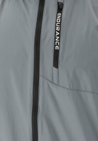 Leichter grauer Windbreaker mit schwarzem Reißverschluss und Branding. Verfügt über eine Reißverschlusstasche und eine glatte Textur, entworfen für den Einsatz im Freien.