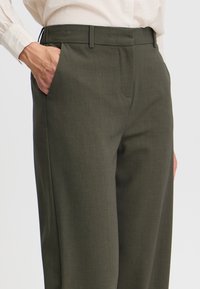 Olivgrüne Hose aus strukturiertem Stoff, mit flachem Bund, seitlichen Taschen und einer taillierten Passform.
