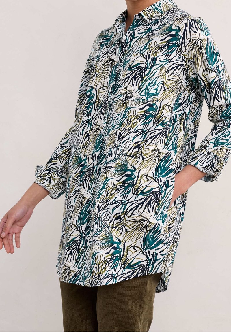 Blumen-Tunika mit Mandarin-Kragen, auf weißem Grund, mit grünen und blauen Blattmustern, langen Ärmeln und seitlichen Taschen.