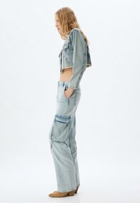 Chaqueta de mezclilla azul claro recortada con dobladillo deshilachado, combinada con pantalones cargo azul claro con bolsillos. El material es suave y la silueta es relajada.