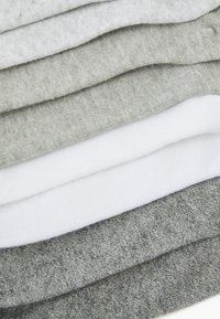 Tessuti misti in cotone di colore bianco, grigio chiaro, grigio scuro e grigio melange, impilati a strati, che mostrano diverse trame e spessori.