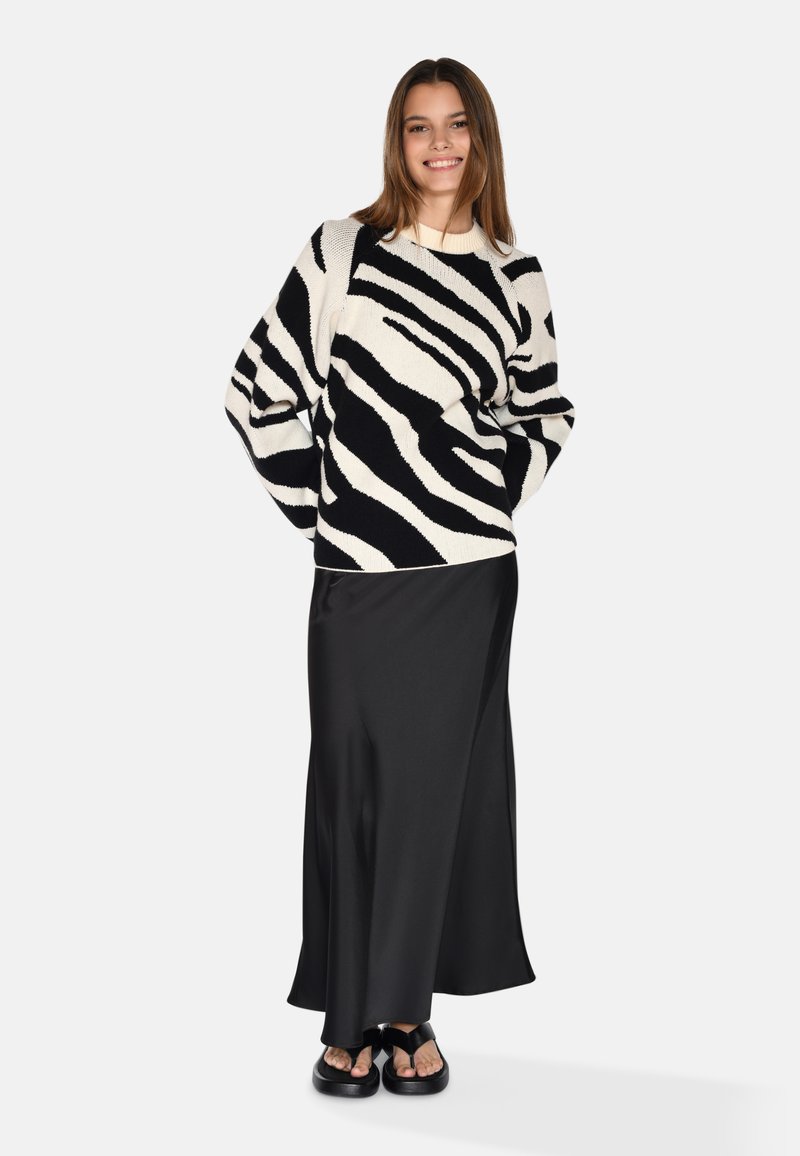 Lange zwarte satijnen rok gecombineerd met een zwart-wit gestreept gebreid sweater. De trui heeft gedurfde zebra-achtige patronen en een ontspannen pasvorm.