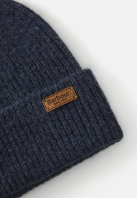 Beanie a costine blu scuro con risvolto, caratterizzato da un piccolo tag in pelle marrone impresso con "Barbour England."