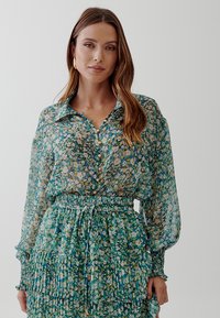 Floral blouse and matching skirt set in green, featuring button closures, elastic waistband, and ruffled tiers. Sheer fabric with colorful patterns.