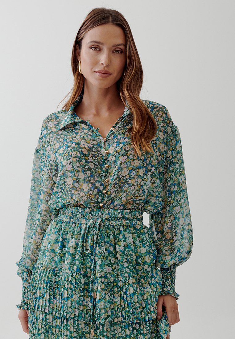 Floral blouse and matching skirt set in green, featuring button closures, elastic waistband, and ruffled tiers. Sheer fabric with colorful patterns.