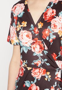 O vestido envolvente floral apresenta um fundo escuro com grandes rosas em tons de rosa, vermelho e aqua. Tem mangas curtas e um decote em V. Textura de tecido suave.