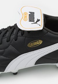 Botín de fútbol negro con parte superior de cuero texturizado, acentos en blanco, logo dorado "KING" y marca PUMA en una etiqueta blanca en el tobillo.