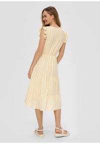 Gelb gestreiftes Midi-Kleid mit Rüschensäulen und gestuftem Rock. Leichter Stoff. Getragen mit neutralen Sandalen. Rückansicht gezeigt.