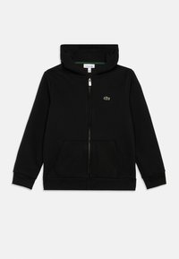 Hanorac negru cu fermoar, fabricat dintr-un material moale, având o suprafață texturată, două buzunare frontale și un mic logo brodat în formă de crocodil, de culoare verde.