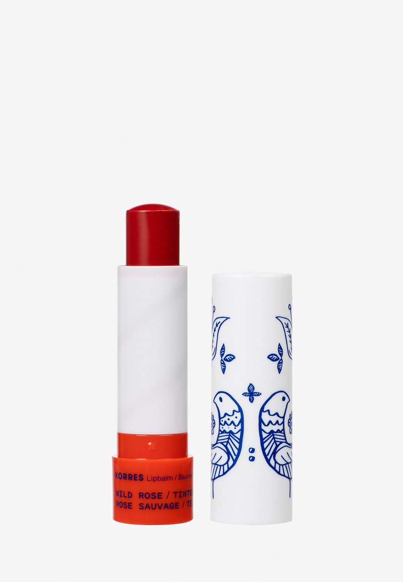 Stick à baume à lèvres avec une teinte rouge, base blanche et orange étiquetée "Korres Wild Rose", et un capuchon blanc ornée d'illustrations d'oiseau bleu et de feuilles.