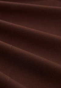 Brauner Stoff mit einer glatten Textur, der weiche Falten und ein konsistentes Webmuster aufweist. Die Farbe ist tief und reichhaltig, typisch für Baumwoll- oder Polyester-Mischungen.