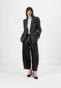 Zwarte gestreepte dubbelknop blazer, lichtblauw aansluitend topje, zwarte nep leren wijde broek, zwarte hoge hakken. Strakke, moderne look.