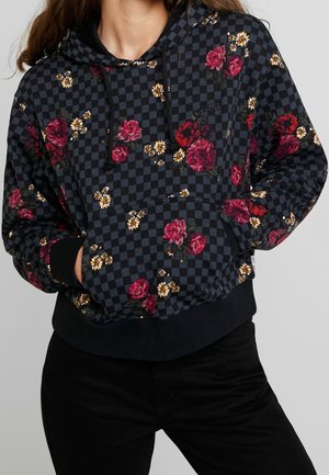 Sort og gråternet hættetrøje med rød og gul blomsterprint, frontlomme, snore, båret af en person med hænderne i lommerne.