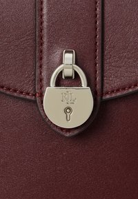 Nahaufnahme einer kastanienbraunen Lederhandtasche mit einem silberfarbenen Vorhängeverschluss, der die eingravierten Initialen zeigt, und einem eleganten Muster sowie einem schlanken Design.