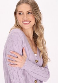 Lila kabelgebreide cardigan met een V-hals, lange mouwen en twee grote knopen. Heeft ribbels aan de mouwen en een zachte textuur.