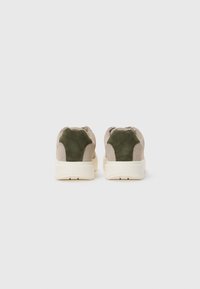 Suede sneakers med en beige og grøn farveskema, der har en chunky hvid sål og subtil branding på hælen. Rundet design.